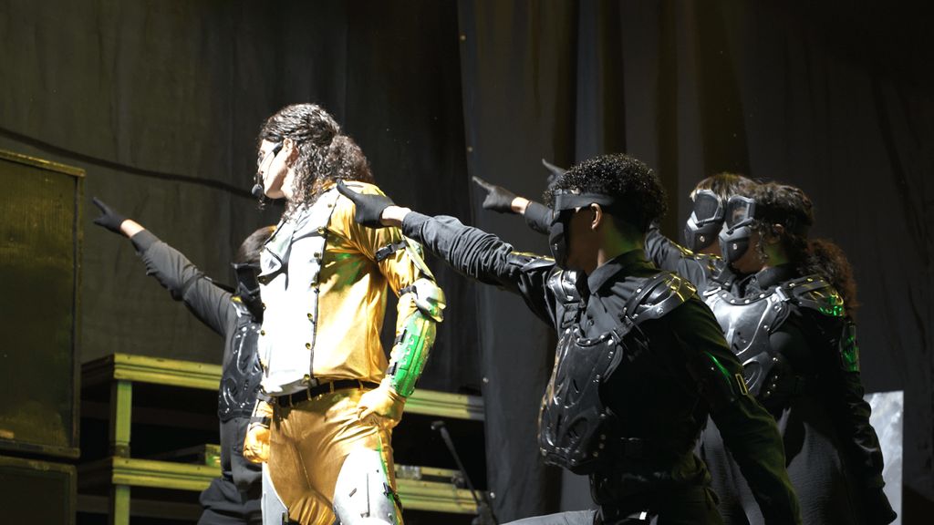 Michael James com figurino dourado e dançarinos